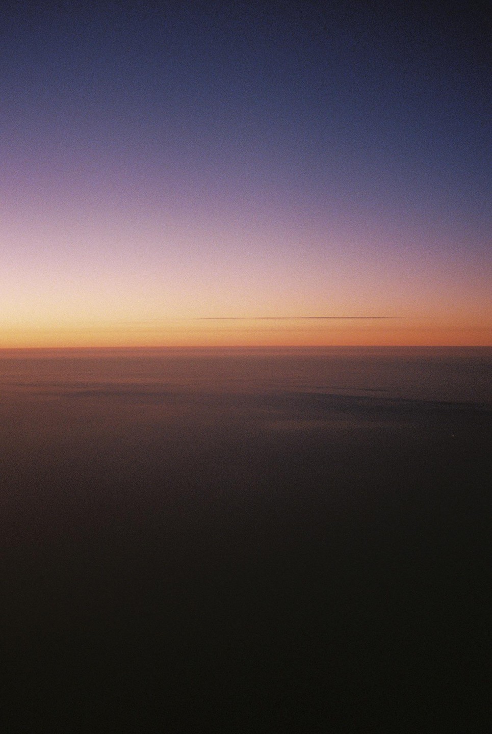 A gradient of purple, orange, and dark blue fills the sky above a dark, hazy horizon.