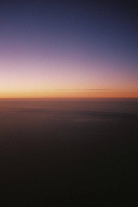A gradient of purple, orange, and dark blue fills the sky above a dark, hazy horizon.