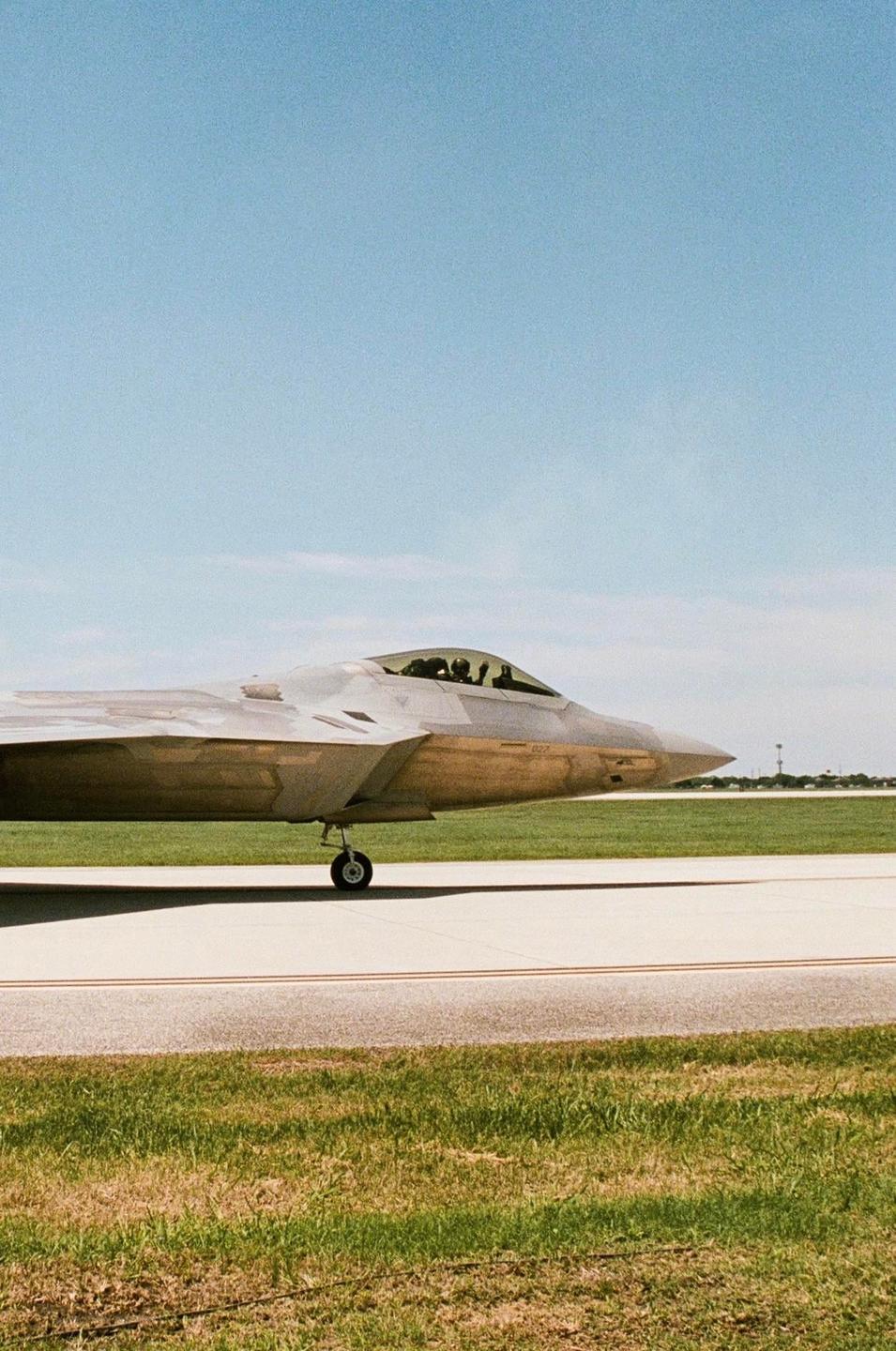 A fighter jet is parked on an airfield with green grass and a clear blue sky.