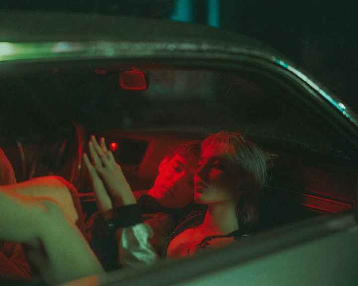 A couple is sitting in a car at night, illuminated by red and green light.