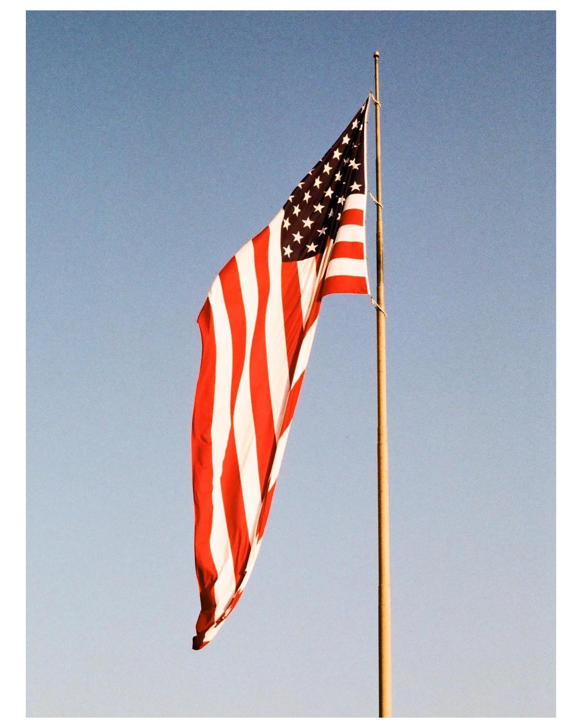 An American flag hangs from a flagpole against a clear sky.