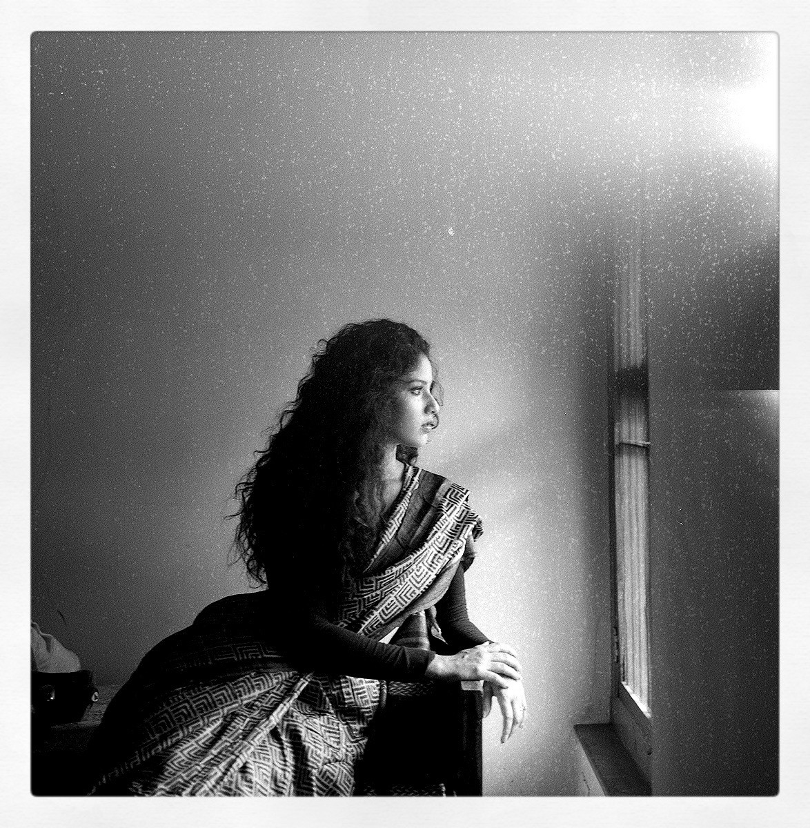 A woman in a sari sits looking out a window.