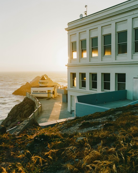 Sunlight reflects off the windows of a large white building next to the ocean, with a smaller building labeled "GIANT CAMERA" visible below.