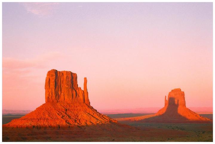 Two large rock formations stand in a desert landscape under a pink and purple sky.