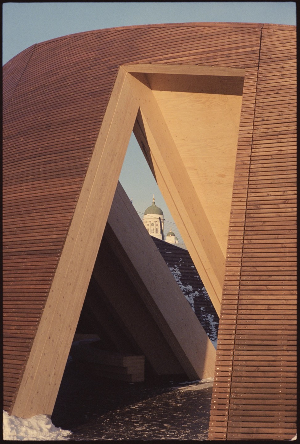 A church dome is visible through a triangular opening in a modern wooden building.