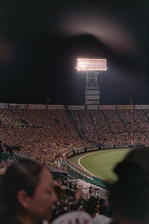 A baseball stadium is illuminated by a bright light tower at night, with a large crowd visible in the stands.