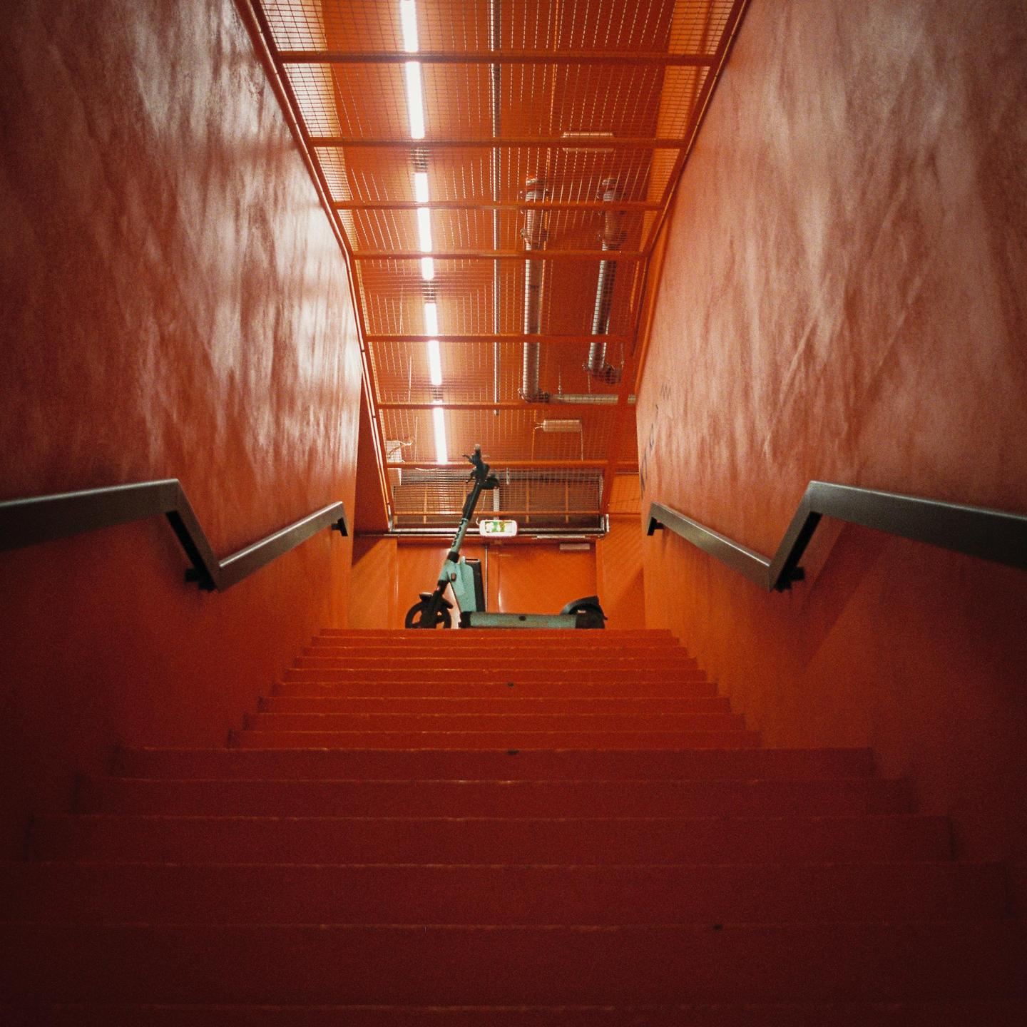 An electric scooter is parked at the top of a long, orange staircase with metal railings.