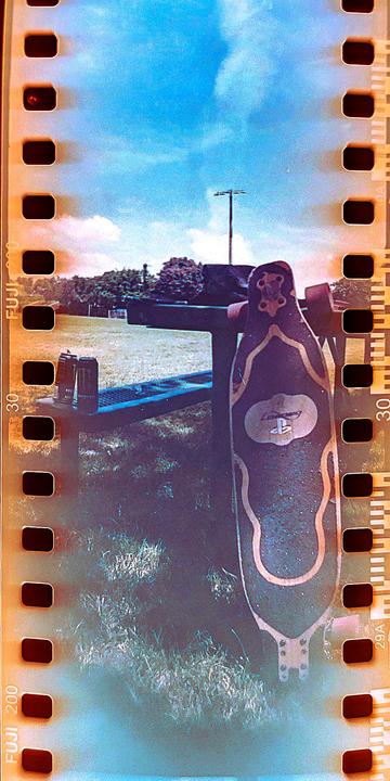 A longboard leans against a picnic table in a grassy field under a bright blue sky.