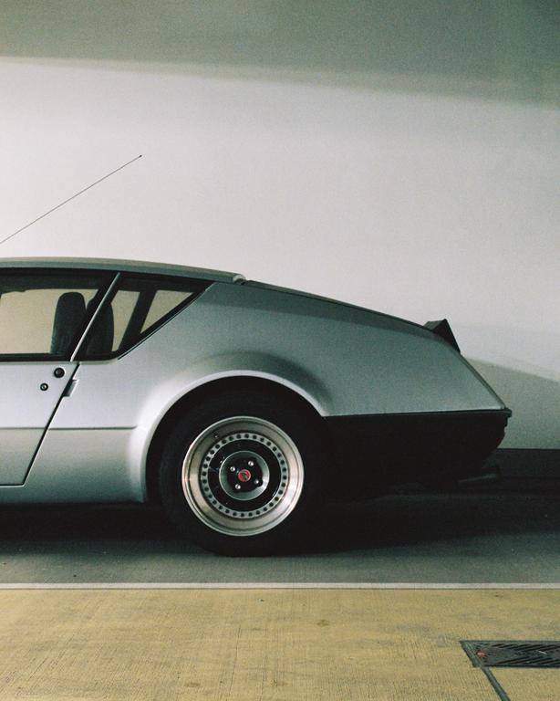 A silver car is parked in a garage, showing its side profile and rear wheel.