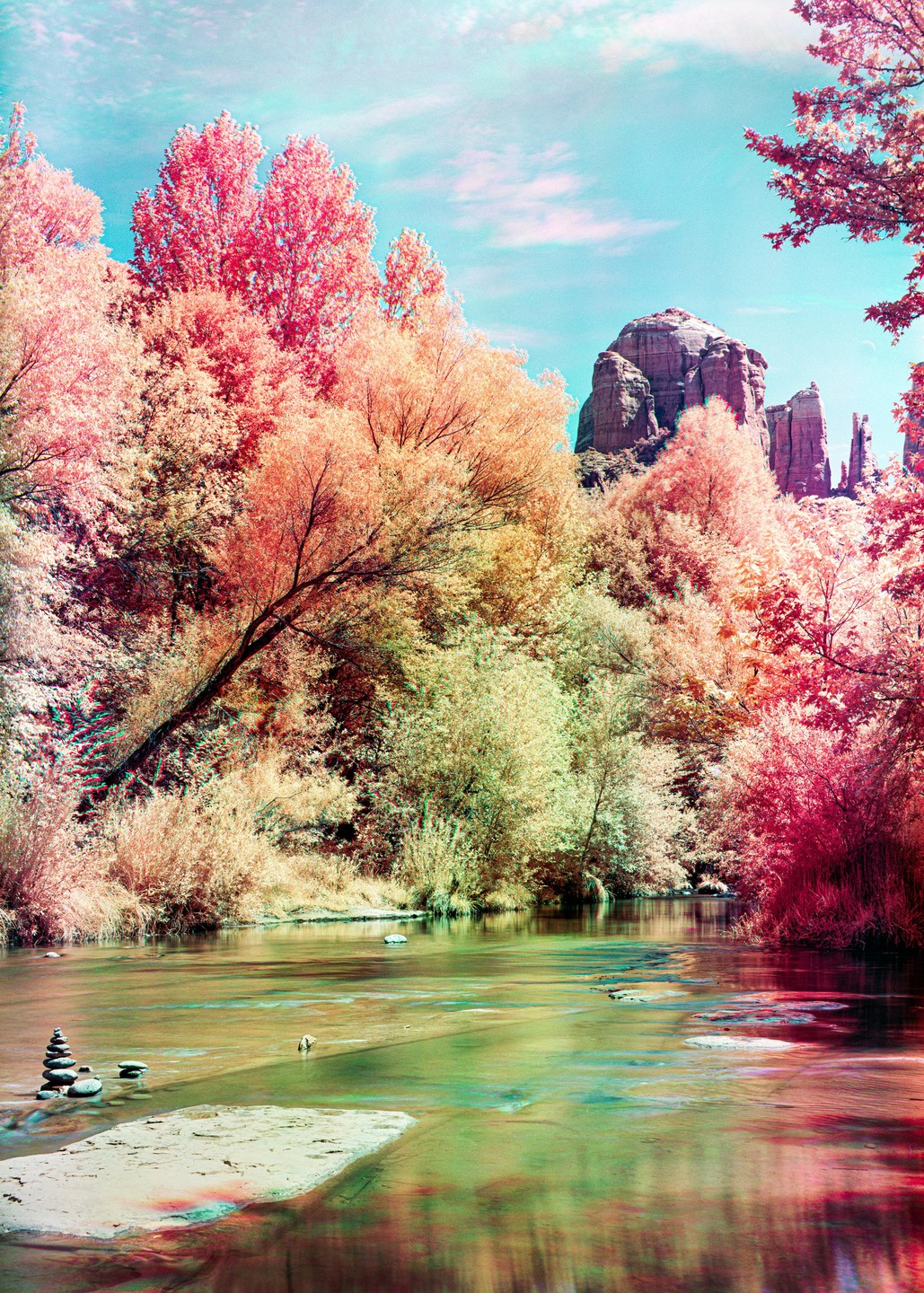A river flows through a landscape with vibrant pink and orange trees under a bright blue sky, with rock formations in the background.