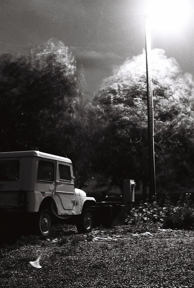 A jeep is parked on a gravel lot next to a bright street light and blurred trees.