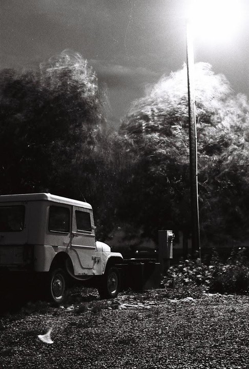 A jeep is parked on a gravel lot next to a bright street light and blurred trees.