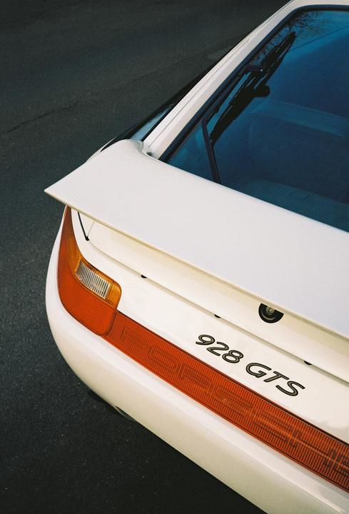 The rear of a white car with orange taillights and a black spoiler is visible.