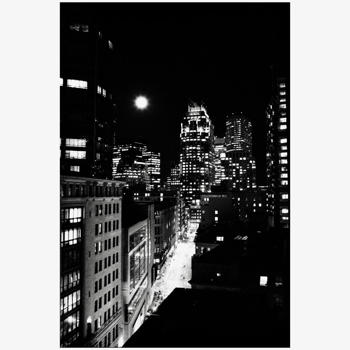 A full moon illuminates a city street lined with buildings at night.
