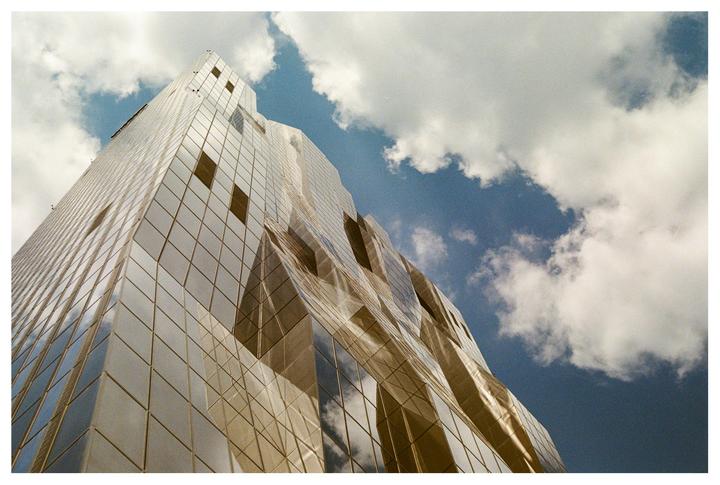 A modern glass building with a geometric facade reflects the sky and clouds.