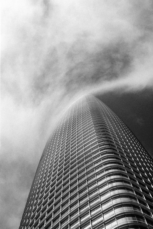 A tall, curved skyscraper rises into a cloudy sky.