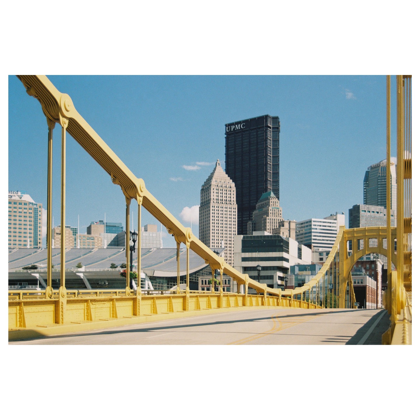 A yellow bridge extends towards a city skyline under a clear blue sky.