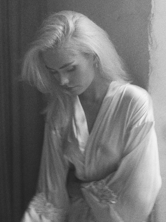 A woman with light hair looks down while wearing a robe.