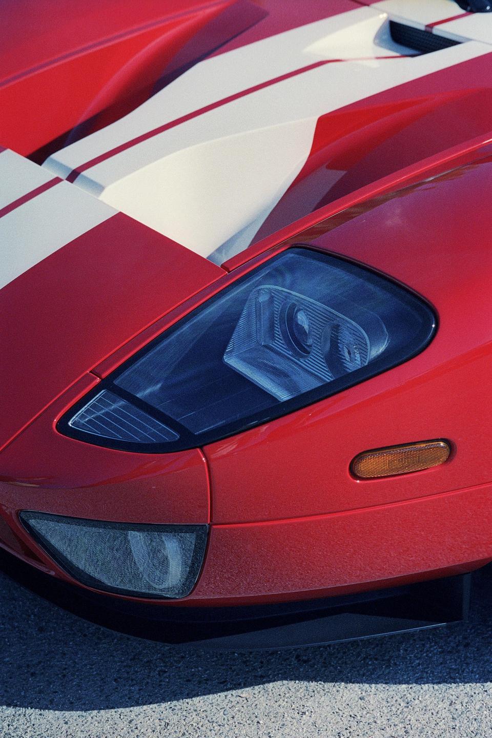 A red sports car with white racing stripes is parked on asphalt.