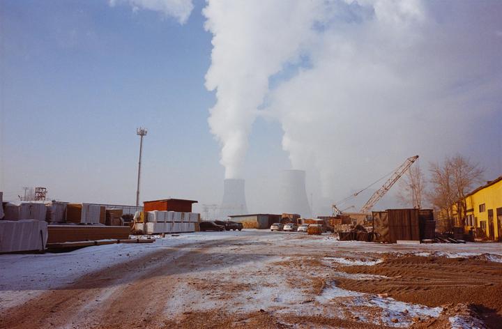 A snowy industrial area with large cooling towers emitting steam into the sky.