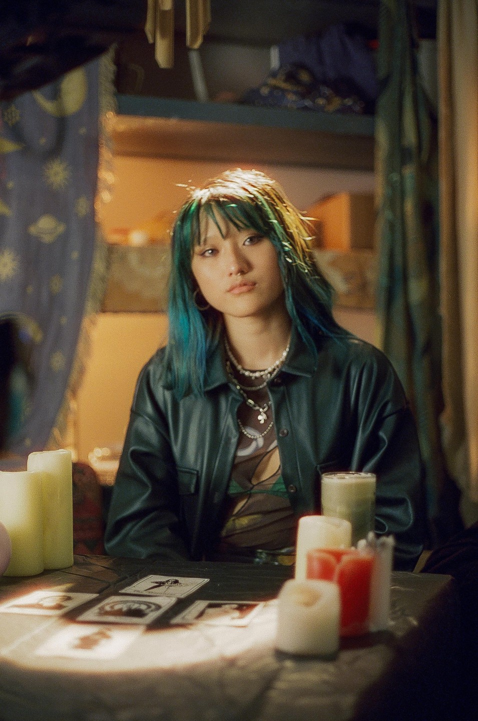 A woman with blue hair sits at a table with tarot cards and candles.