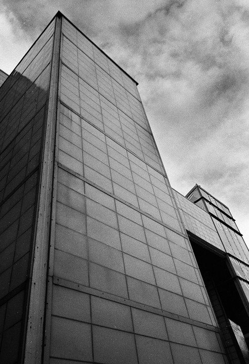 A low-angle view shows the facade of a modern building with a cloudy sky above.