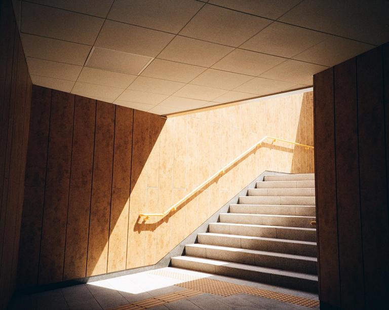Sunlight illuminates a subway staircase with a yellow handrail.