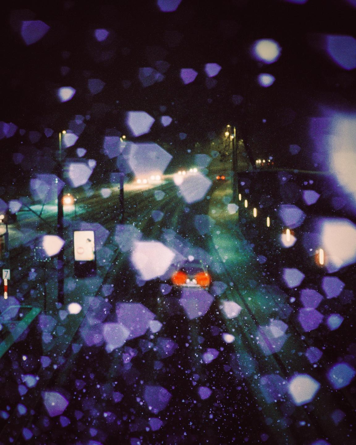 A blurry night street scene shows cars and streetlights through a window covered in purple and white bokeh.