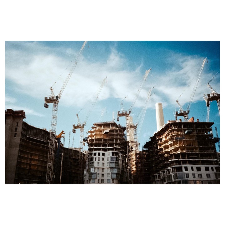 Several cranes tower over buildings under construction against a blue sky with clouds.