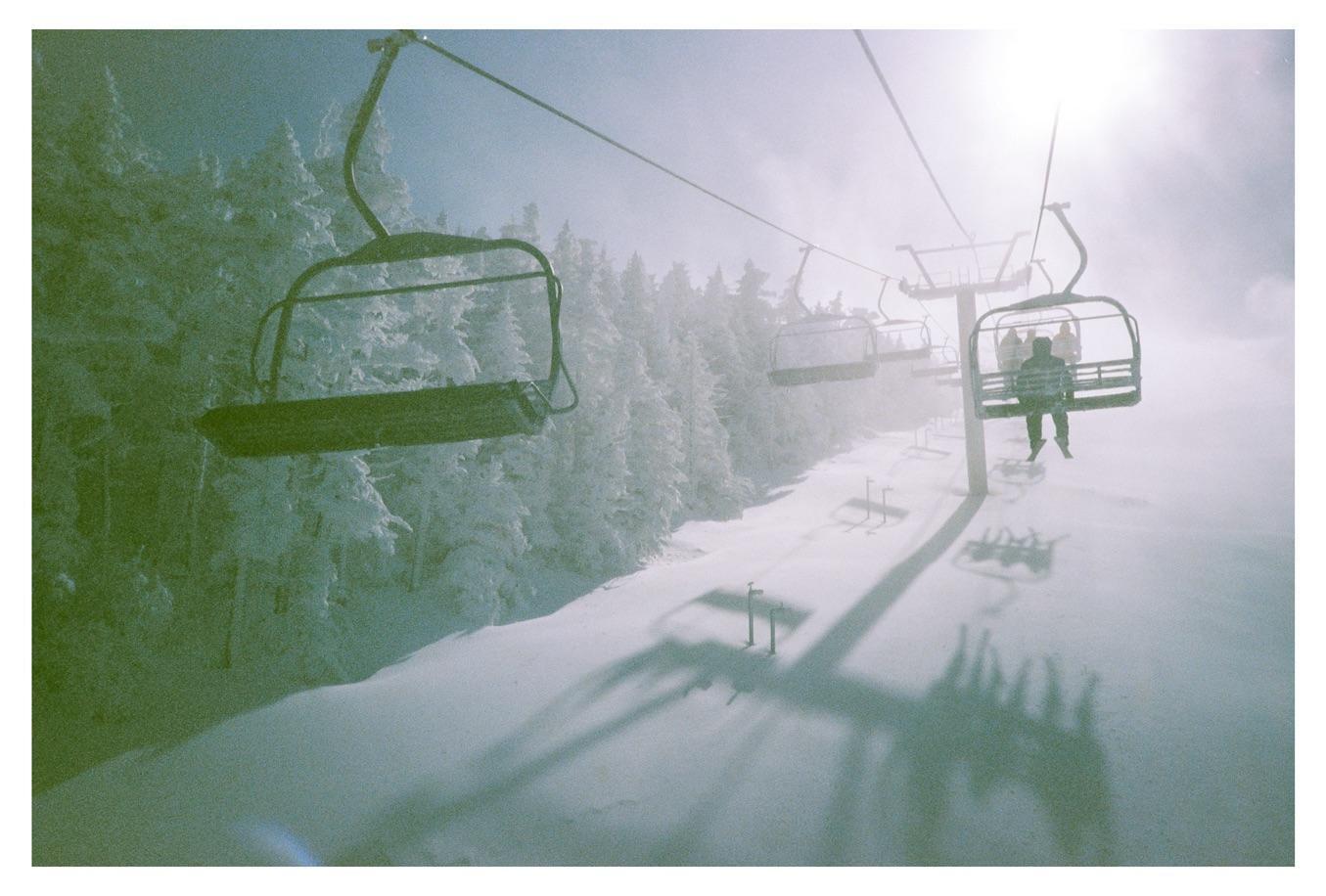 A person rides a ski lift over a snowy mountain with trees covered in snow.