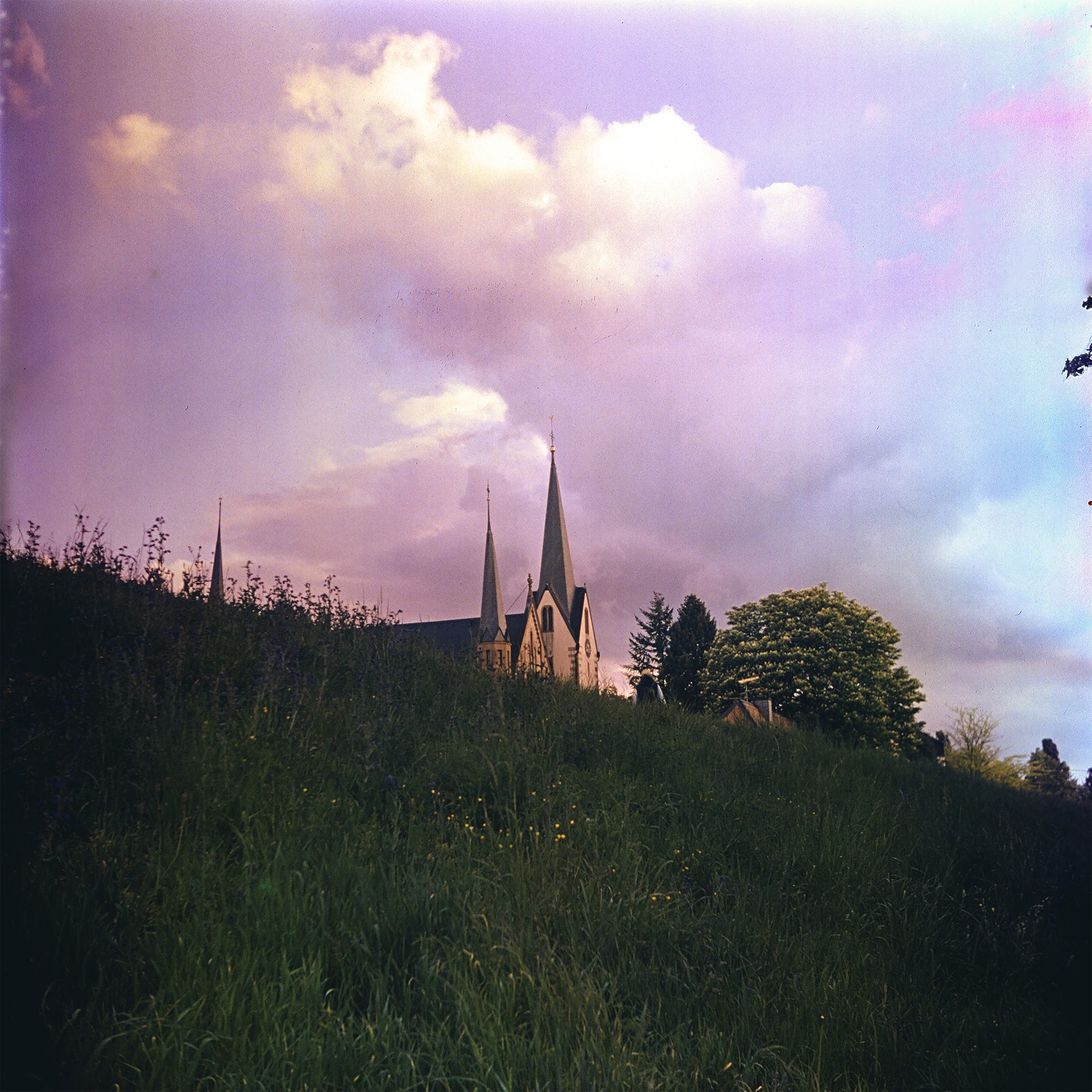 A church with two spires is visible on a hill under a cloudy sky.