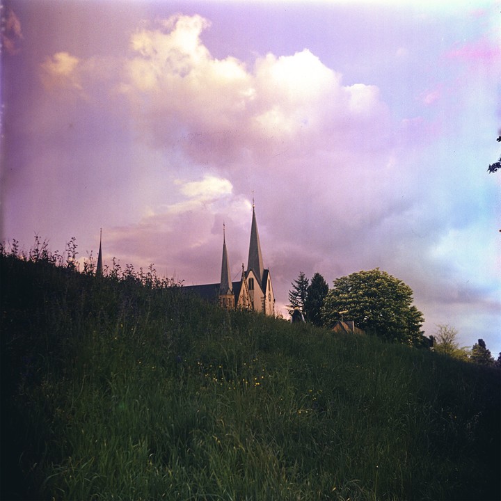 A church with two spires is visible on a hill under a cloudy sky.