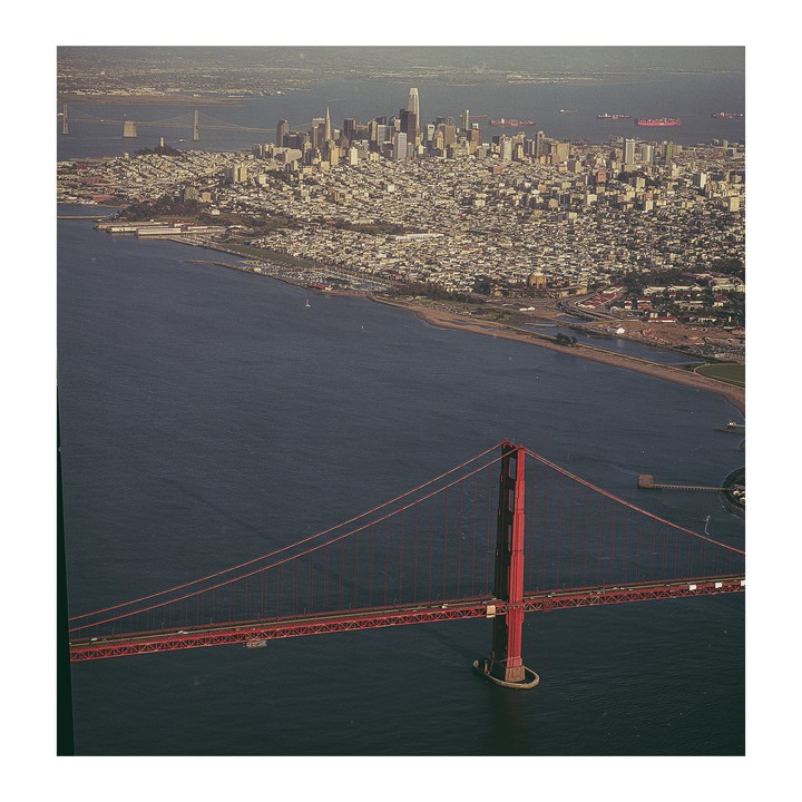 An aerial view shows the Golden Gate Bridge in the foreground with the San Francisco skyline and bay in the background.