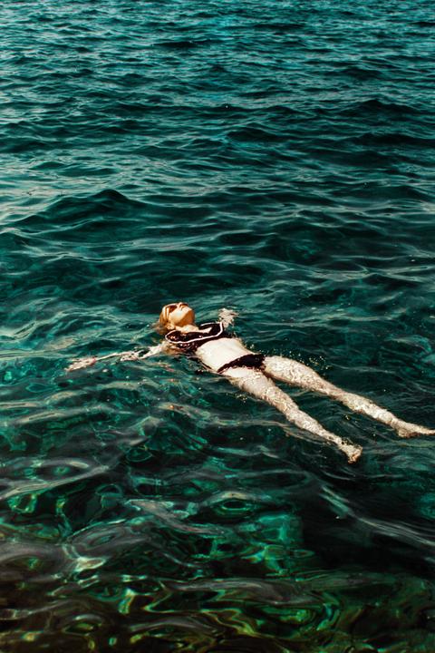 A woman floats on her back in clear blue-green water.