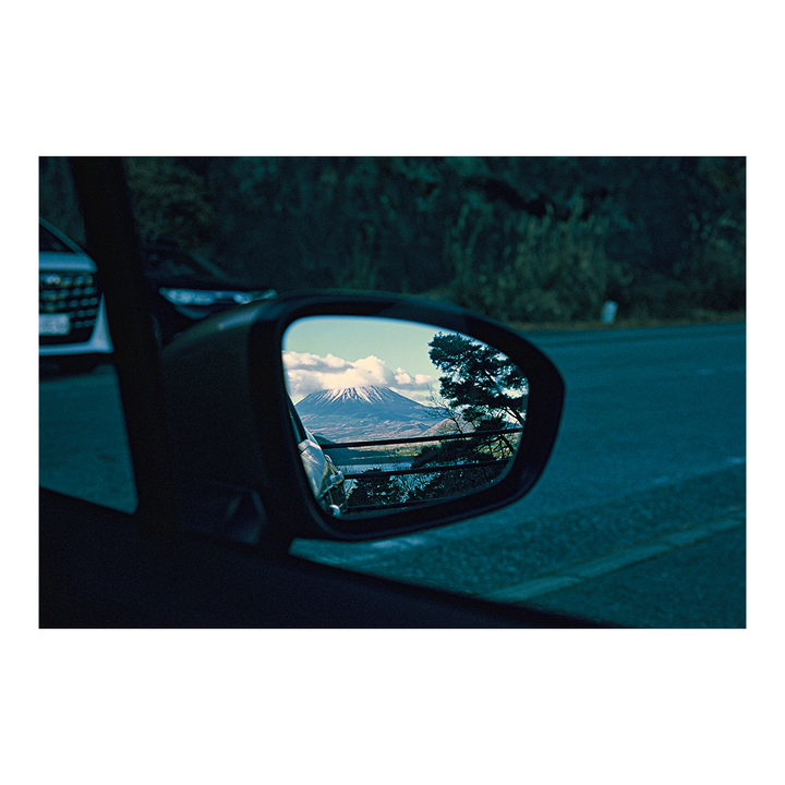 A snow-capped mountain is reflected in a car's side mirror.