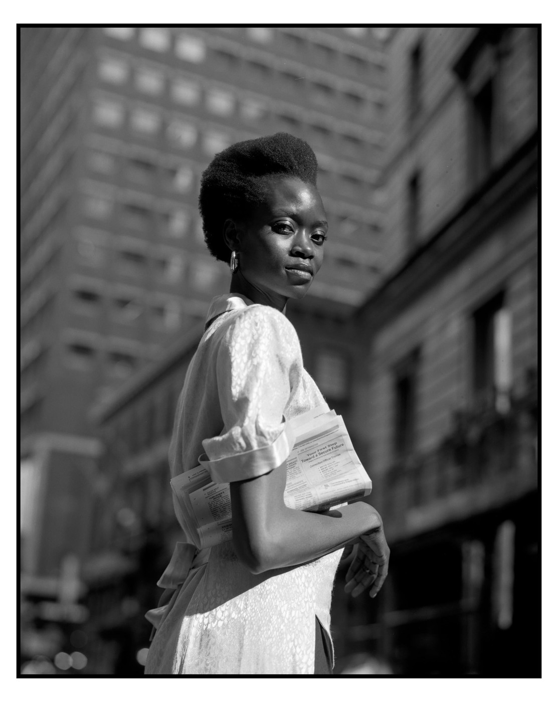 A woman with papers tucked under her arm looks over her shoulder on a city street.