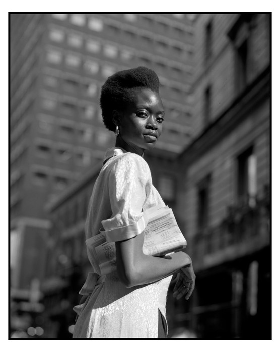 A woman with papers tucked under her arm looks over her shoulder on a city street.