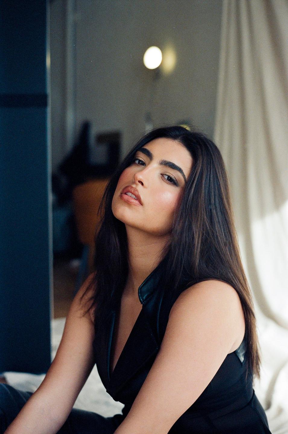 A woman with long dark hair and a black top looks directly at the viewer.