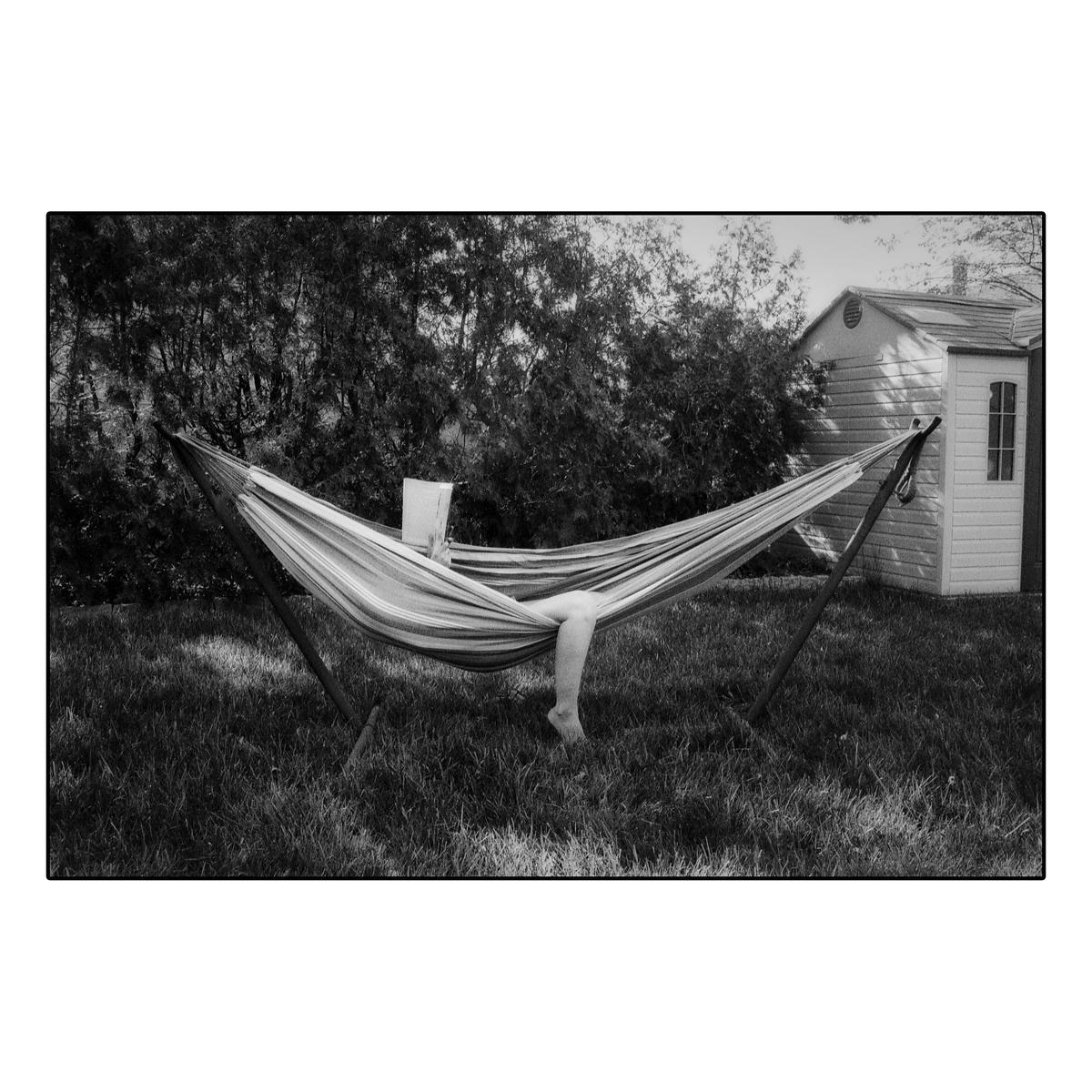 A person is relaxing in a hammock in a grassy yard with a book.
