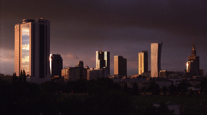 A city skyline with tall buildings is visible under a dark sky, with some buildings reflecting light.