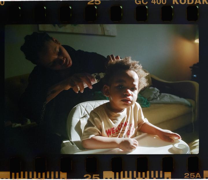 A woman applies product to a child's hair while the child sits in a high chair.