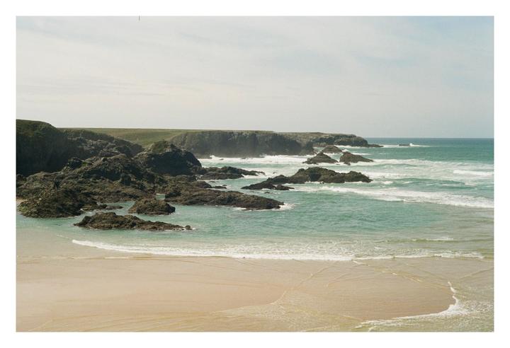 A sandy beach with turquoise water and rocky outcrops is visible under a bright sky.