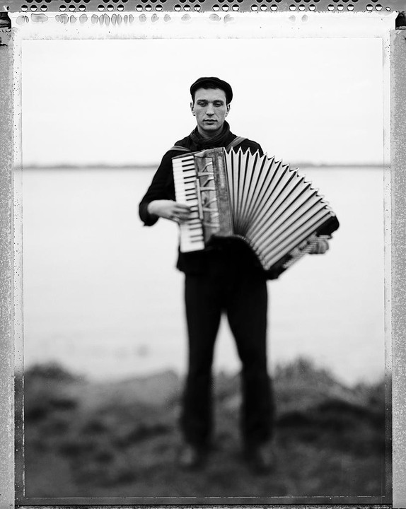 A man wearing a beret plays an accordion outdoors.