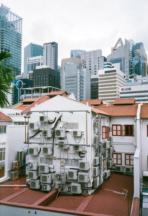 A building with many air conditioning units on its exterior stands in front of a city skyline.