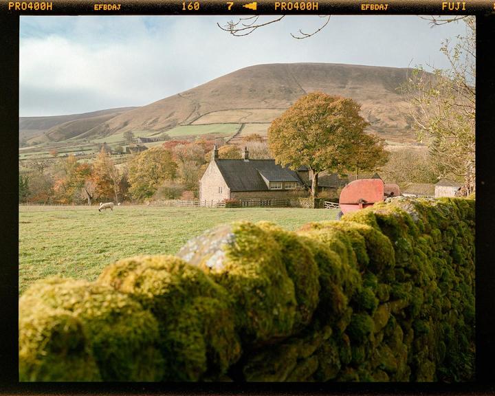 A moss-covered stone wall is in the foreground of a house and rolling hills.