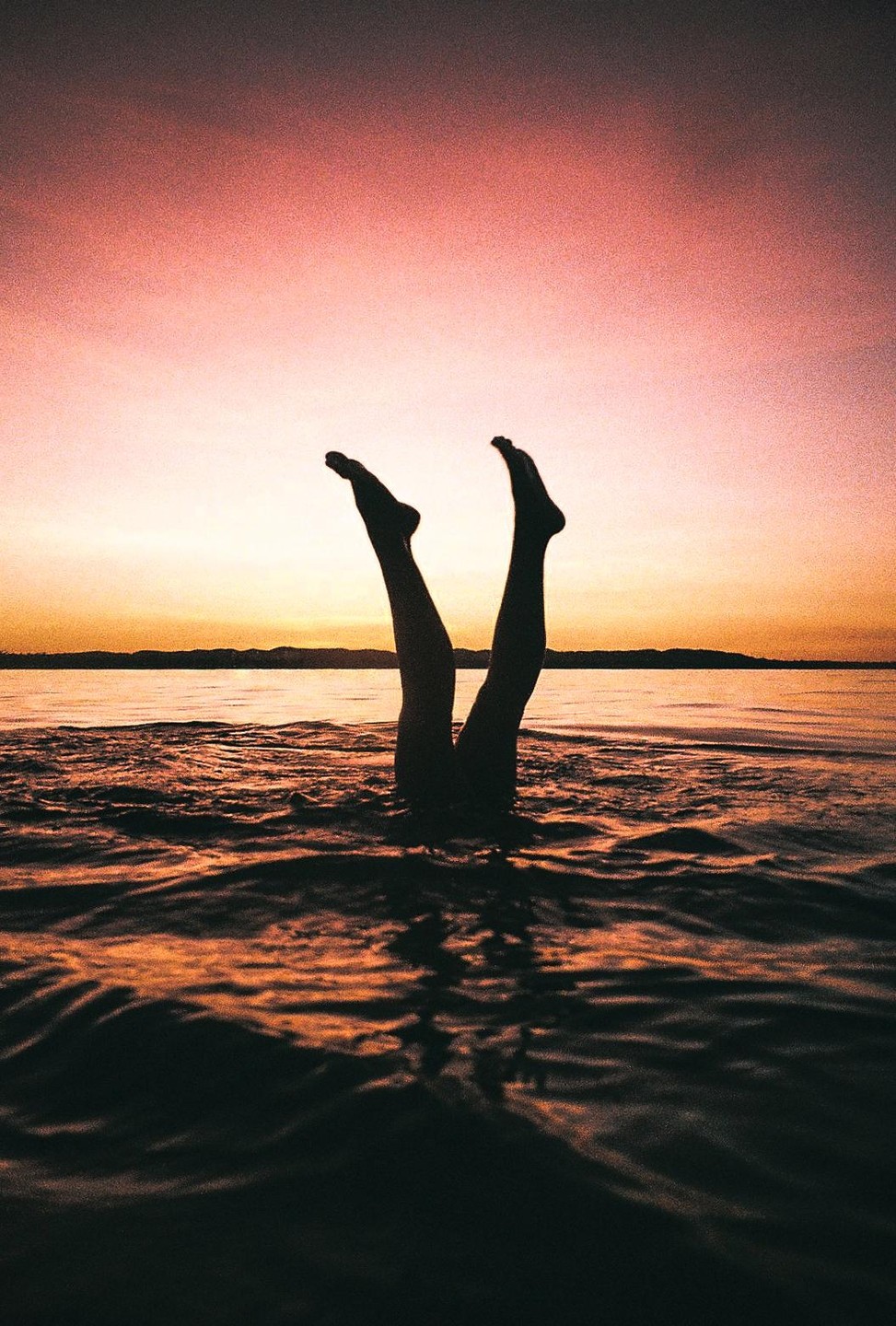 Two legs stick out of the water at sunset.