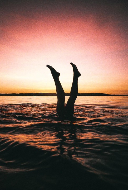 Two legs stick out of the water at sunset.