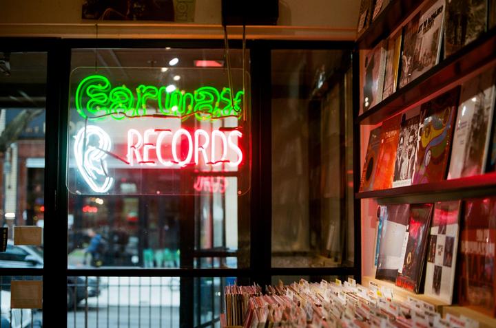 A neon sign for "Earwax Records" is visible through a window, with records displayed on shelves inside.