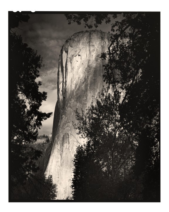 A large rock formation is framed by dark trees and foliage.