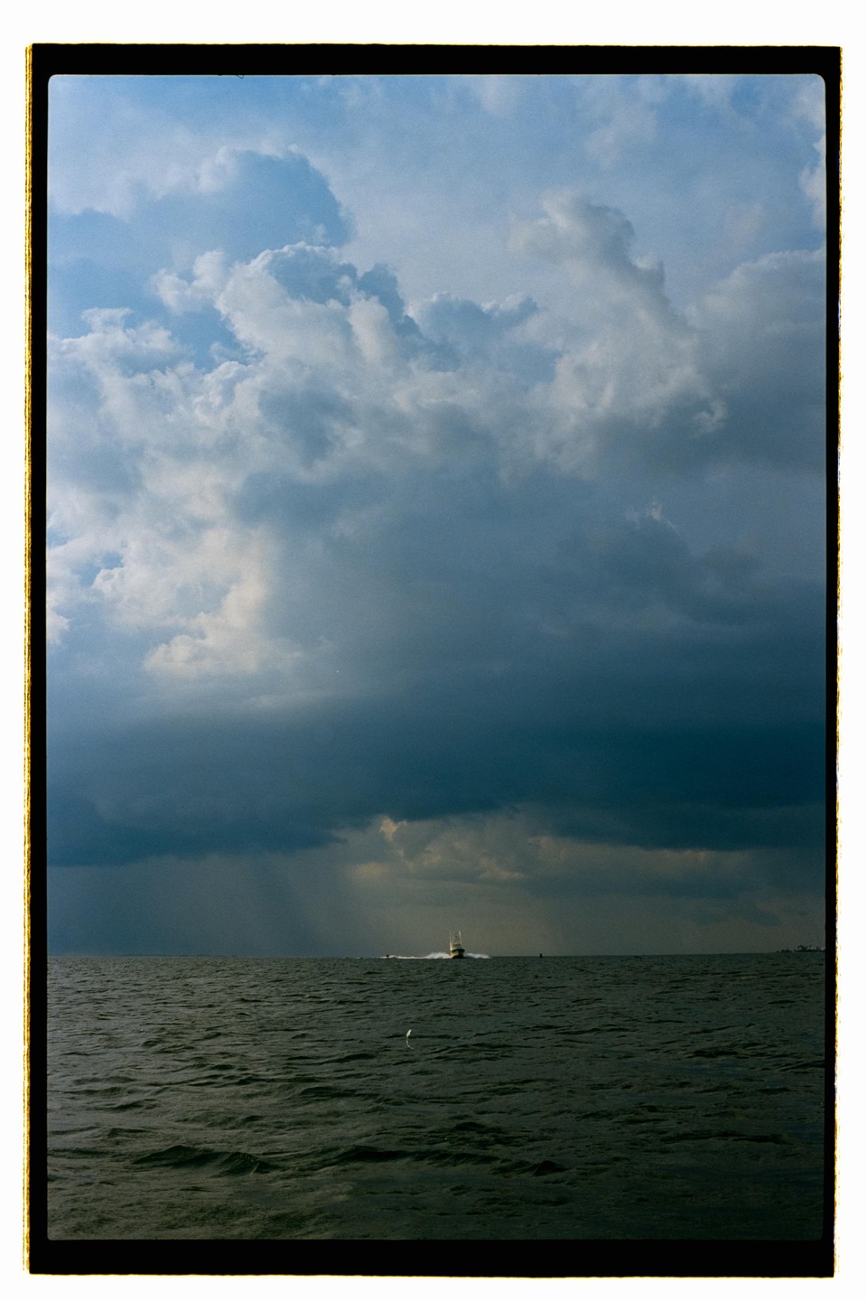 A boat moves across the water under a dramatic sky with rain falling in the distance.